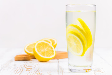 A glass beaker and a jug of cold lemonade on a white wooden background surrounded by lemons.