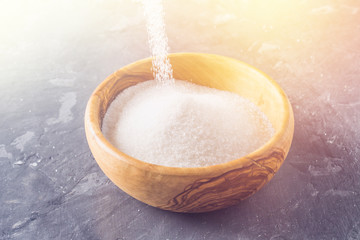 Sugar grains pouring and overflowing a bowl.