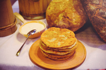  pile of air pancakes on a wooden dinette, a traditional food family. pancakes of golden color, sour cream in the background