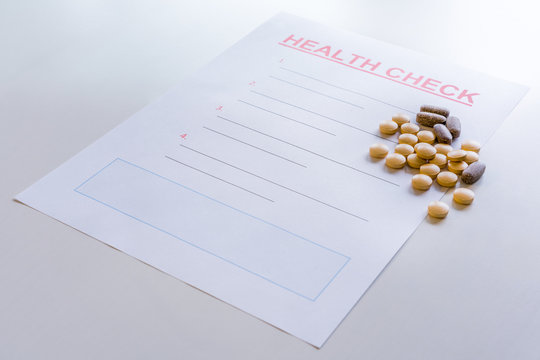 A blank health check form with medicine, vitamins, pills scattered on it.