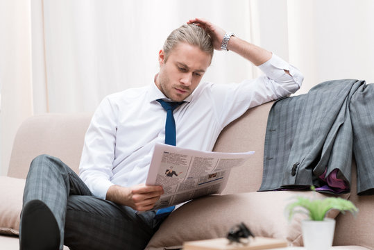 concentrated businessman reading newspaper on sofa at home