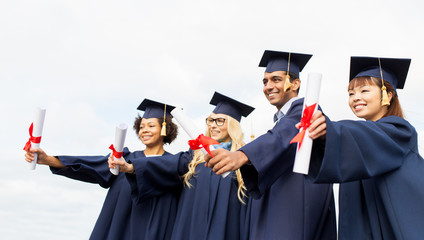 happy students in mortar boards with diplomas
