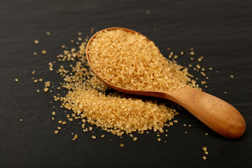 Wooden spoon of brown cane sugar on black slate