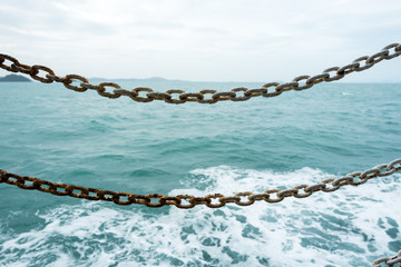 Rusty chains used to protection and obstruction passengers falling from ship over blue sea background.