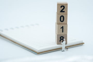 2018 New year concept.  Painter miniature figure standing and painting number on wooden blocks on notebook with white background.