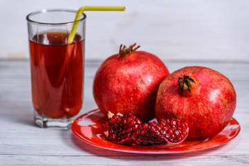 glass beaker with pomegranate juice and pomegranate fruits on a light wooden background