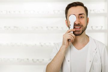 portrait of positive man optometrist check vision closing eye with with diagnostic tool. On the...