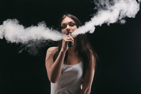 Young woman vaping e-cigarette with smoke on black