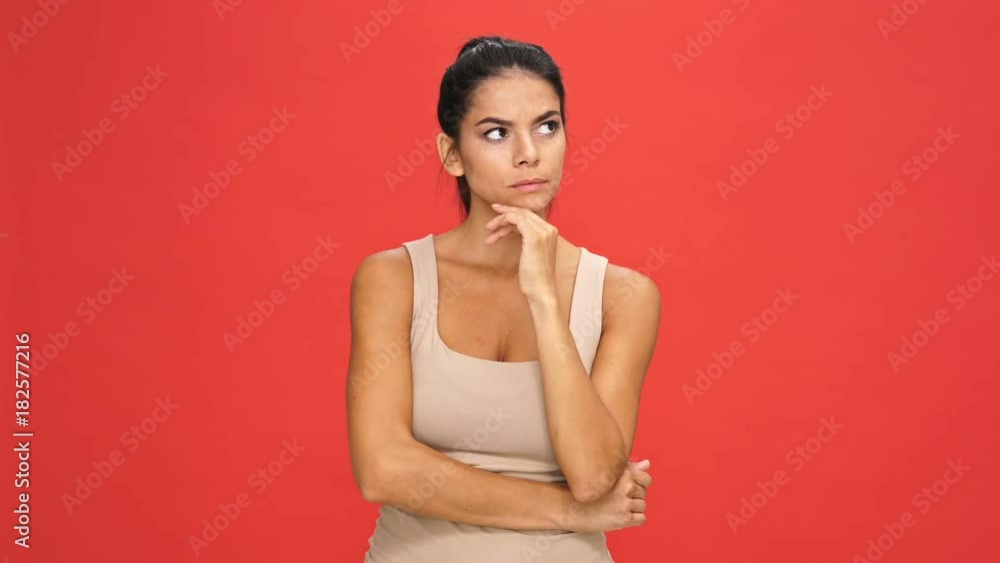 Poster pensive brunette woman in singlet looking around over red background