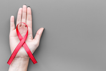 Hand hold red ribbon for HIV, AIDS, substance-abuse and anorexia awareness on grey background top view copyspace
