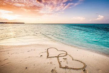 Twee harten getekend op een zandstrand aan zee.