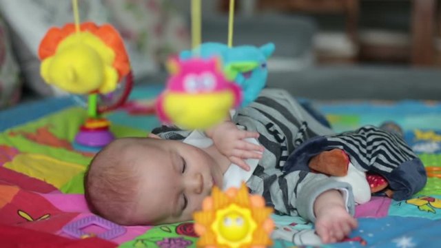 Happy three months old baby boy, playing at home on a colorful activity blanket, toys and different activity around him
