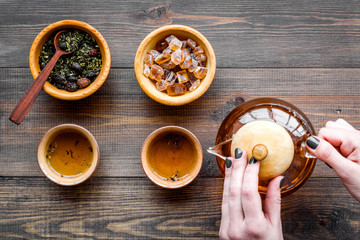 Pour tea from tea pot. Cups, dry tea leaves on dark wooden background top view copyspace