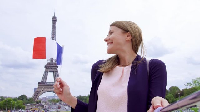 Woman with small French flag near Eiffel Tower in Paris, France doing selfie on mobile phone with selfie-stick. Happy smiling tourist woman traveling in Europe.