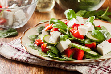 Fresh spinach salad with feta, cucumber and red paprika on a plate.