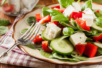 Fresh spinach salad with feta, cucumber and red paprika on a plate.