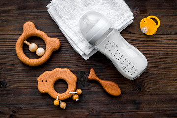 Baby accessories. Wooden toys, pacifier and bottle on dark wooden background top view