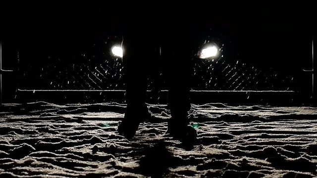 Snow falls in the headlights, walking feet into dark night shot in slow motion. mystery person background.