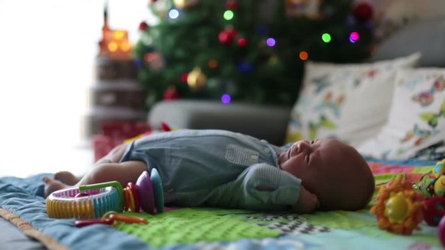 Three months old baby boy, crying at home on a colorful activity blanket, toys and different activity around him