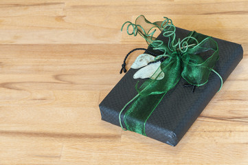 Gift in front of wood background / Gift in black paper with green bow in front of wood background.