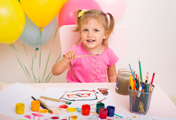 A little girl at the table and drawing with watercolors