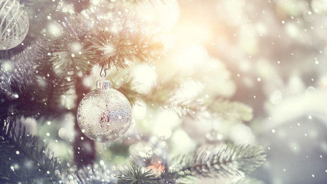 Silver and white bauble hanging from a decorated Christmas tree with bokeh and snow, copy space. Xmas holiday background.