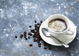 Cup of coffee on a table and beans scattered around. Winter background.