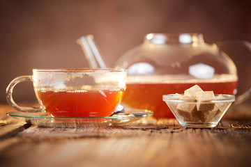 Hot black tea in  glass cup and teapot with brown sugars cubes