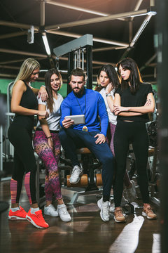 Smiling personal trainer using digital tablet while talking to group of women