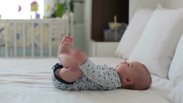 Cute little smiling newborn baby boy, playing in bed in the morning, rolling over, baby activity