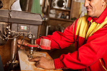 carpenter using drill press to mae hole in wooden plank