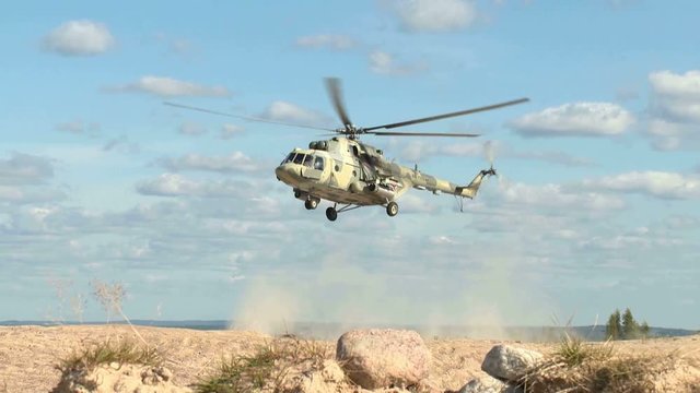 A Russian military helicopter is landing in a desert area, raising clouds of dust.