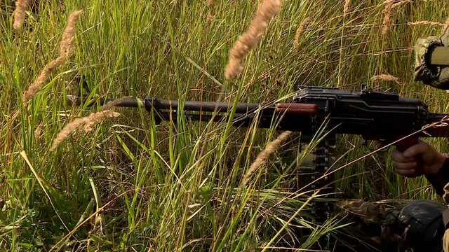  	A machine gunner in a helmet and camouflage takes aim and fires a machine gun, the machine gunner conducts targeted fire from cover.