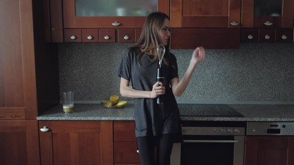 funny girl fooling around singing in a blender instead of a microphone, sings in the mixer, attractive young brunette with glasses long hair and loose clothing has fun and dancing in the kitchen