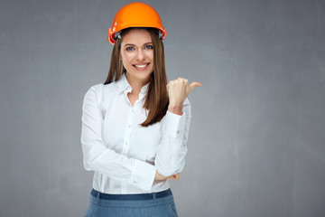Smiling businesswoman wearing builder helmet pointing thumb finger at side.
