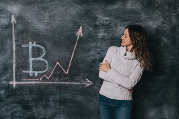 Girl watching the chart of bitcoin exchange rate drawn on black chalkboard with chalk