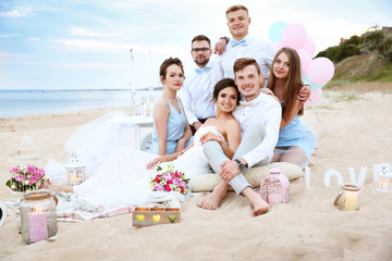 Happy wedding couple with friends on beach