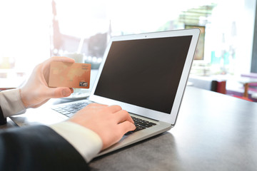 Young man using laptop and credit card for online shopping at table