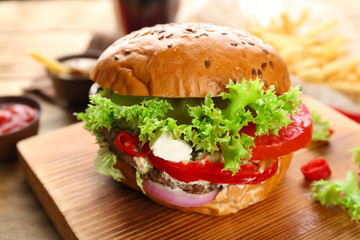 Wooden board with fresh tasty burger on table