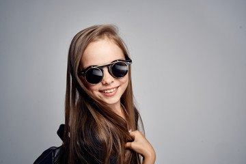 young girl in black and glasses smiles against a gray background