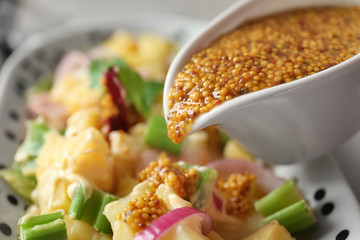 Pouring mustard sauce into bowl with potato salad, closeup