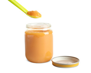 Spoon and jar with healthy baby food on white background