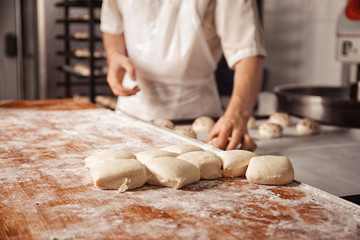 Raw buns on table and man in bakery