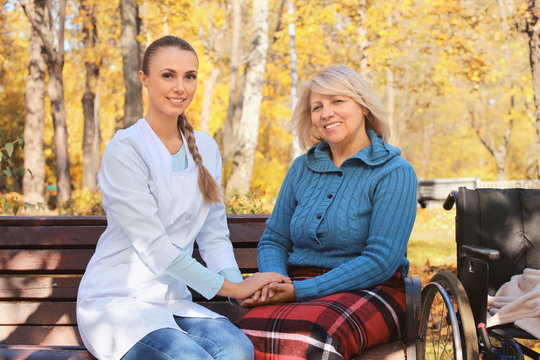 Senior woman and young nurse sitting on bench in park