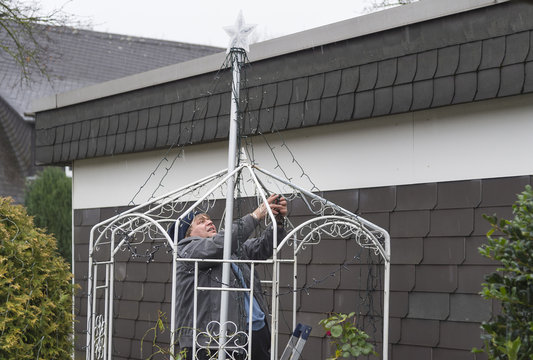 Mann dekoriert den Garten mit Lichterketten w&auml;hrend es regnet