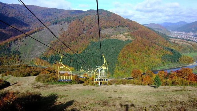 4K UHD footage of ski lift or elevator going down with empty seats over colorful autumn mountain landscape background