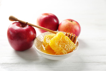 Honeycomb in bowl and apples on wooden table