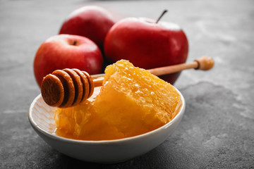 Honeycomb in bowl and apples on gray table