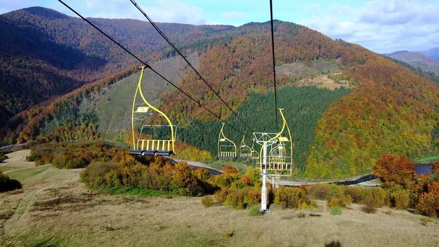 4K UHD footage of ski lift or elevator going down with empty seats over colorful autumn mountain landscape background