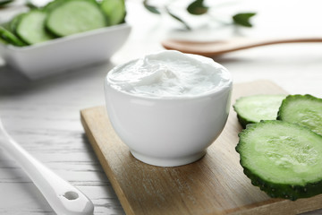Obraz na płótnie Canvas Bowl of body cream with sliced cucumber on wooden board